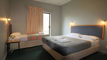 Une chambre d’hôtel avec deux lits, une fenêtre avec des rideaux, une table de chevet avec une plante et des lampes fixées au mur.