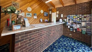 A reception area with a wooden ceiling, a brick counter, and a bulletin board with various notices. - Pelicans Motel San Remo (San Remo)