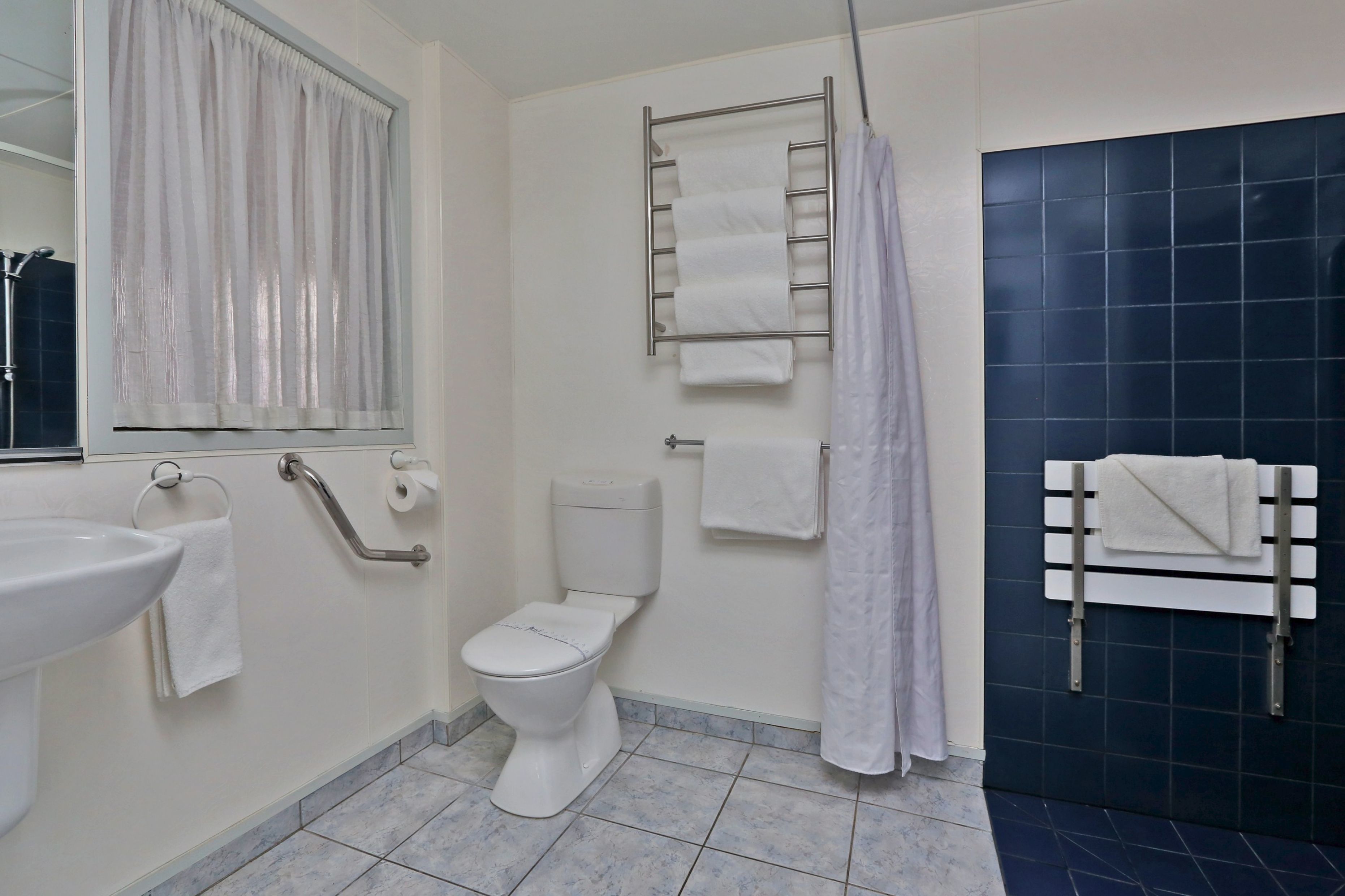 Un baño con inodoro, lavamanos, toallero y cortina de ducha.