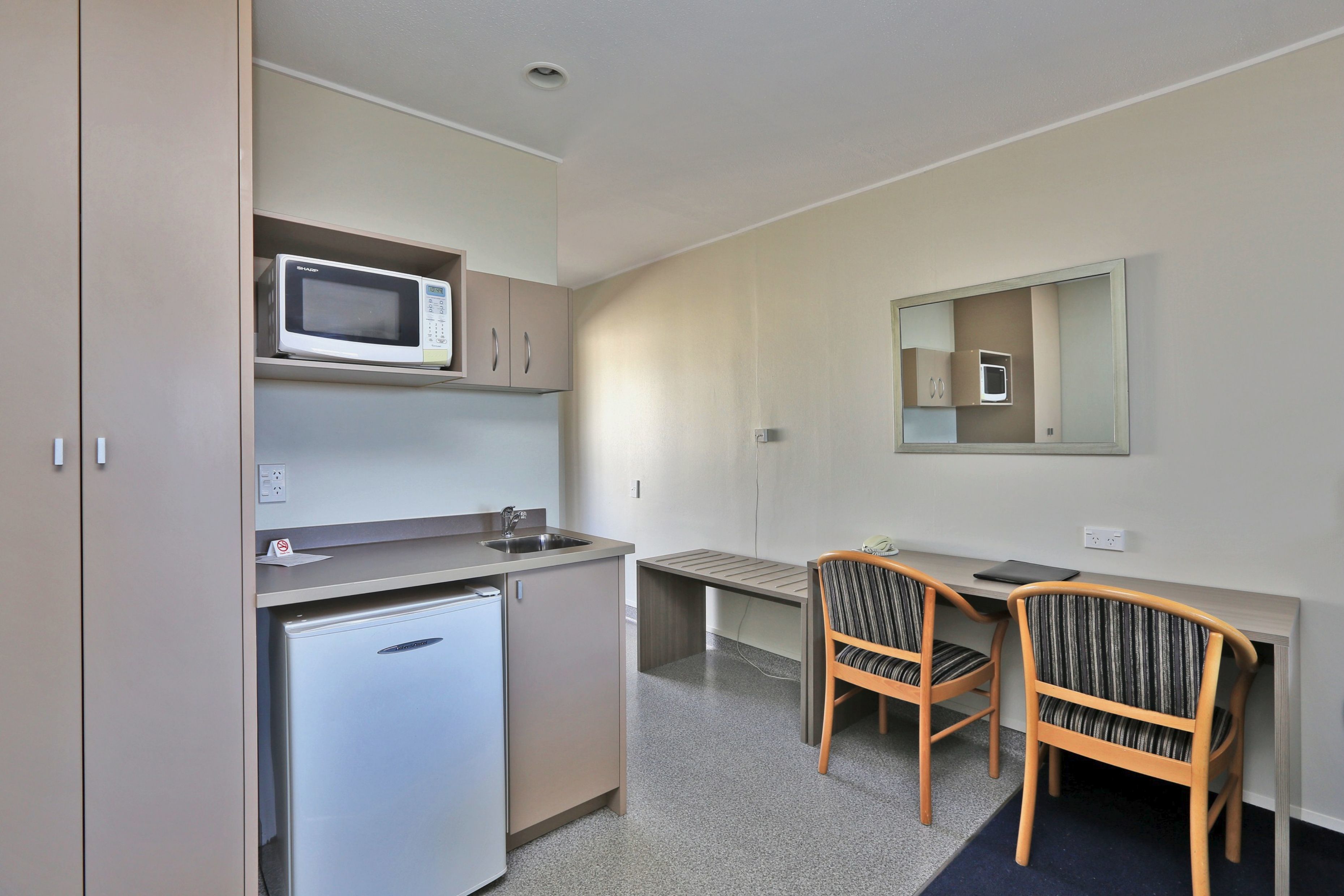 A compact kitchenette with a microwave, refrigerator, and sink. There are two chairs and a small table.
