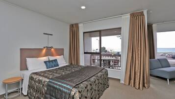 A hotel room with a bed, a small table, a sofa, and a large window with curtains.