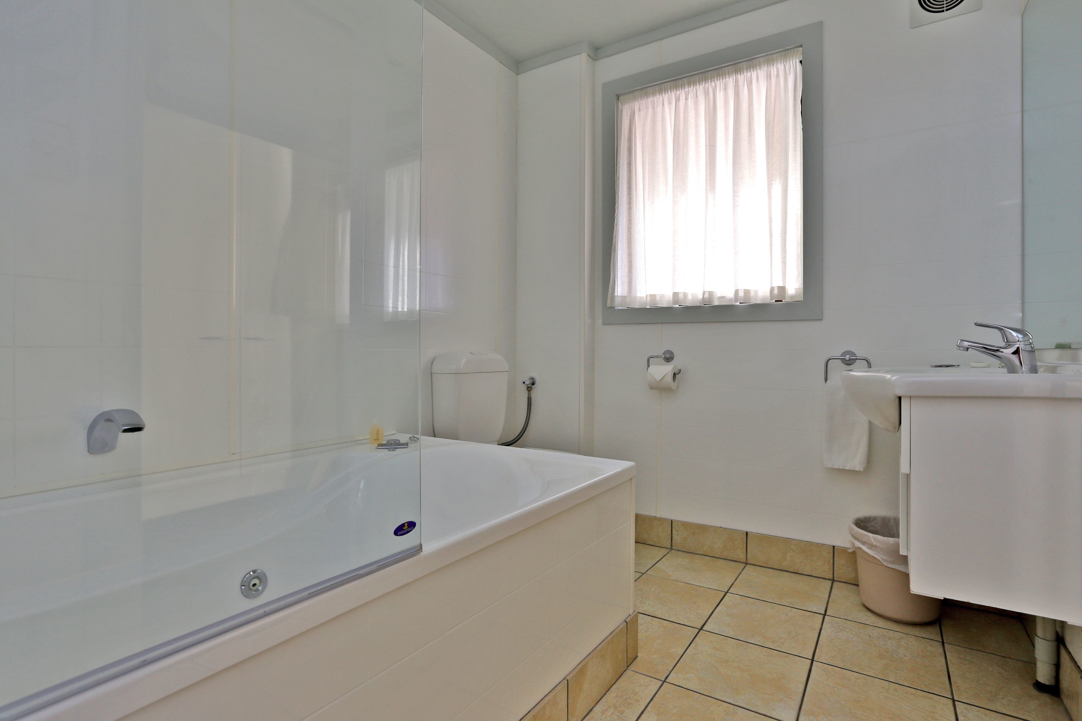 Ein modernes Badezimmer mit einer großen Badewanne, einem Waschbecken und einem Fenster mit Vorhängen.