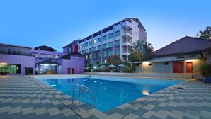 A swimming pool with a ladder, surrounded by a checkered floor, and adjacent buildings with balconies and outdoor lighting. - Aston Tanjung City Hotel (Murungpudak)
