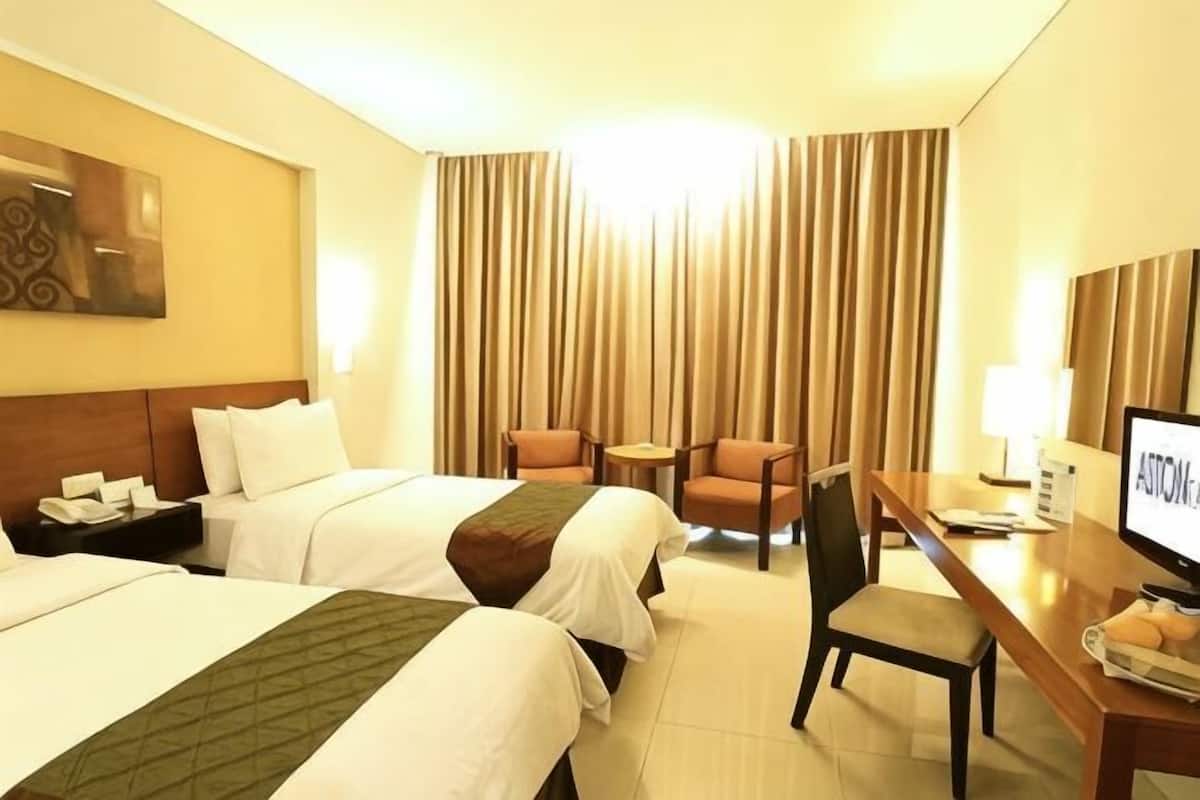 A hotel room with two beds, a desk, a chair, a television, and a window with curtains.