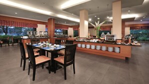 A modern dining area with a central buffet station, multiple seating arrangements, and a view of the outdoors. - Aston Tanjung City Hotel (Murungpudak)