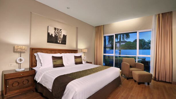 A hotel room with a large bed, a wooden nightstand, a desk, and a view of the outdoors. - Aston Tanjung City Hotel (Murungpudak)