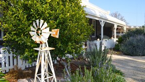 Un molino de viento en un jardín con una valla blanca y un edificio al fondo.
