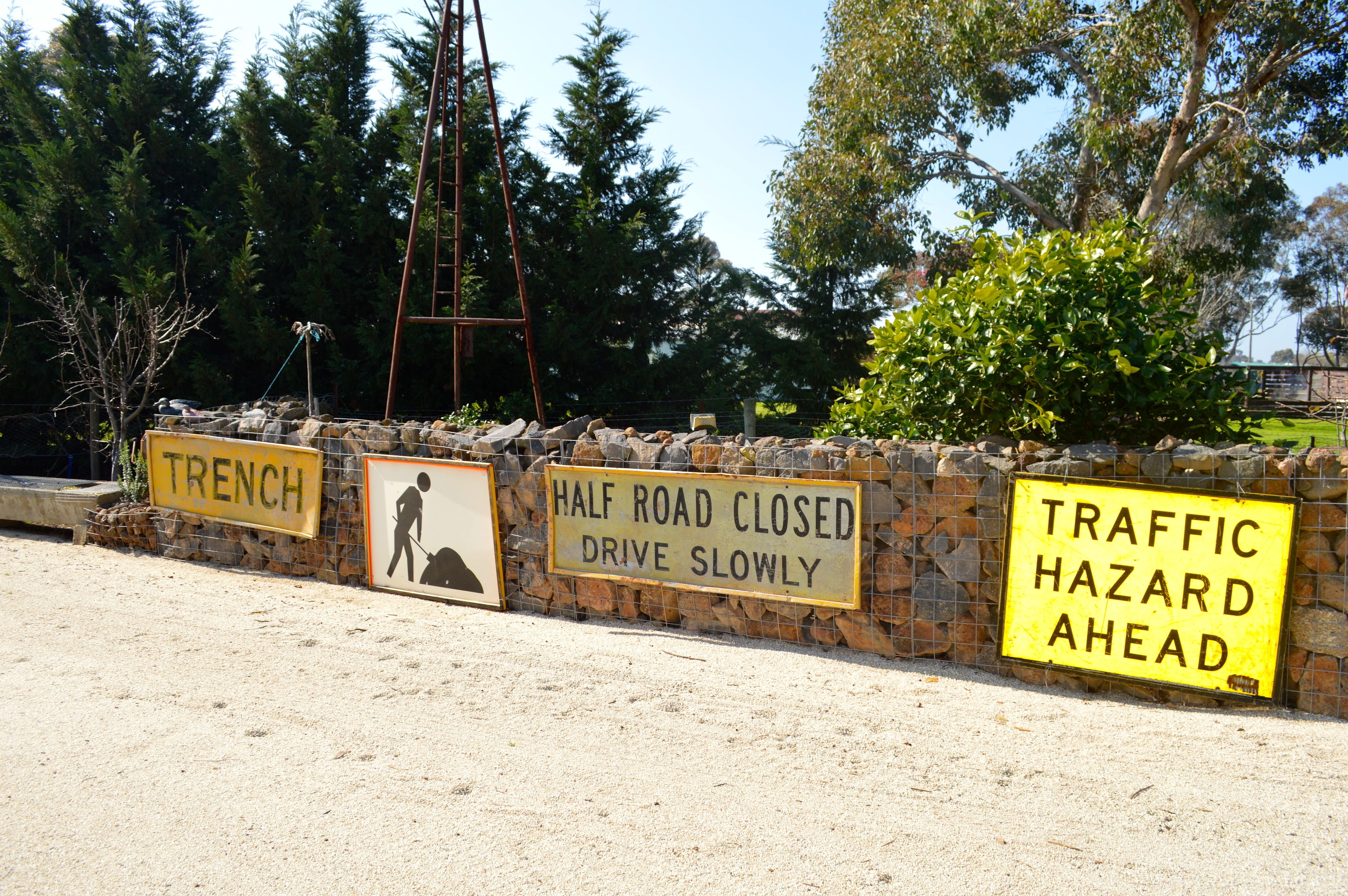 A construction site with warning signs including 'TRENCH', 'HALF ROAD CLOSED', and 'TRAFFIC HAZARD AHEAD'.