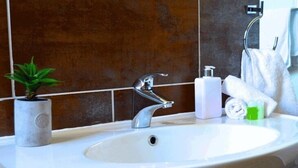 Un baño con un lavamanos blanco, grifo cromado y una planta en maceta.