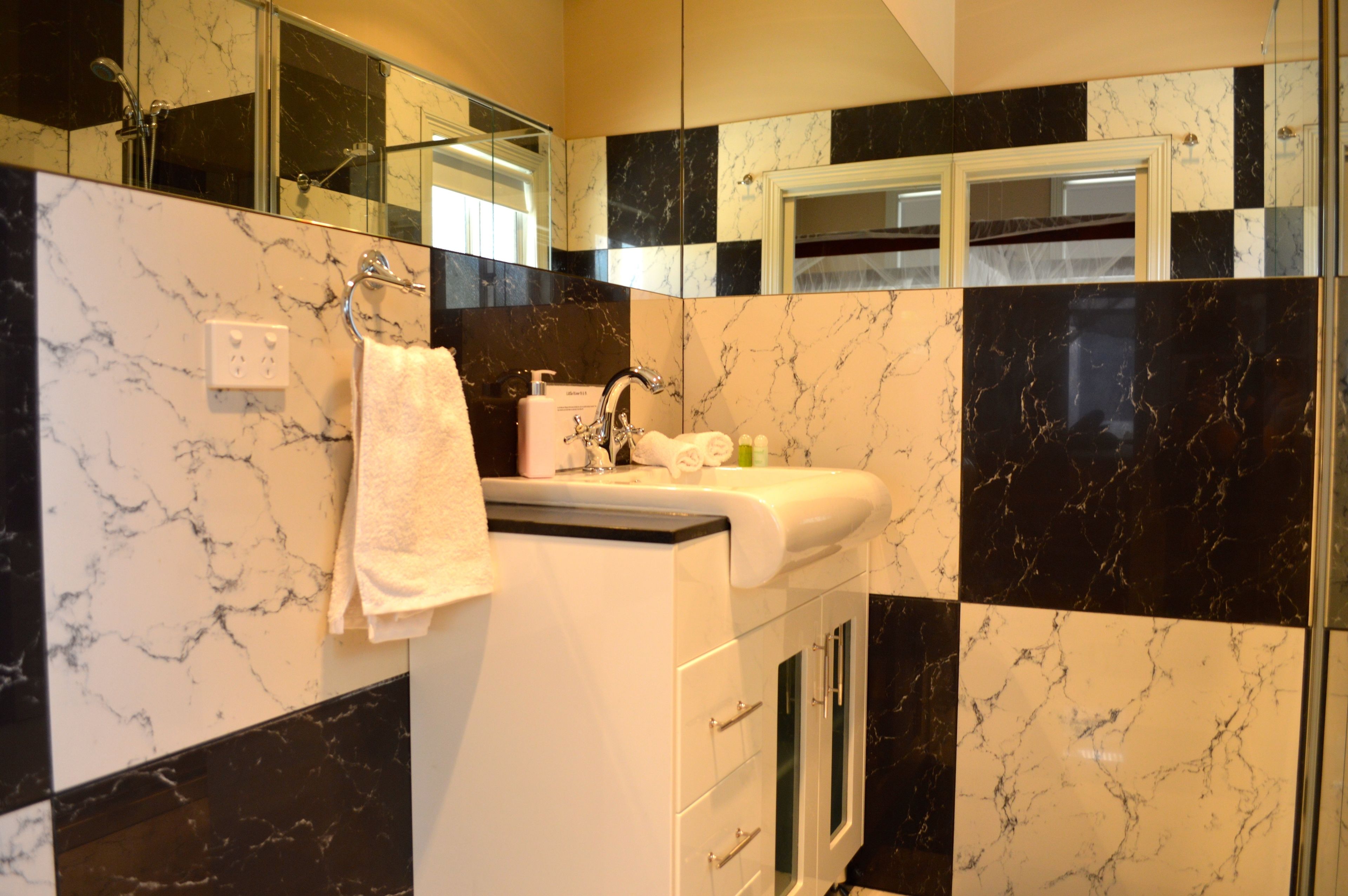 Un baño con un lavamanos blanco, paredes de mármol blanco y negro, un espejo y un perchero para toallas.