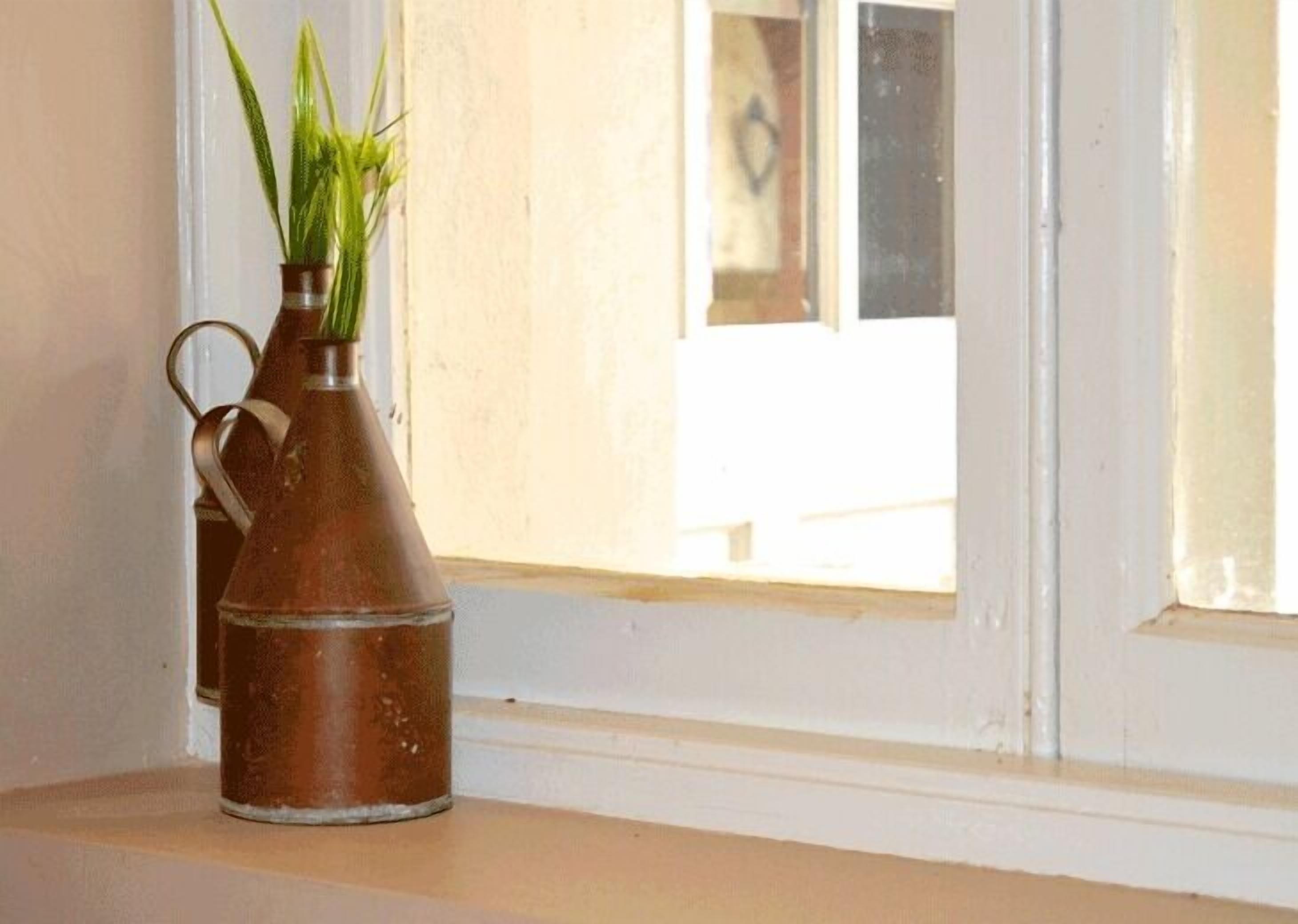 A metal vase with a handle on a windowsill.