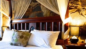 Una cama con sábanas blancas, un cojín estampado y un cabecero de madera.