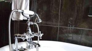 Un baño con una bañera cromada, un cabezal de ducha de mano y una toalla colgada en un perchero.