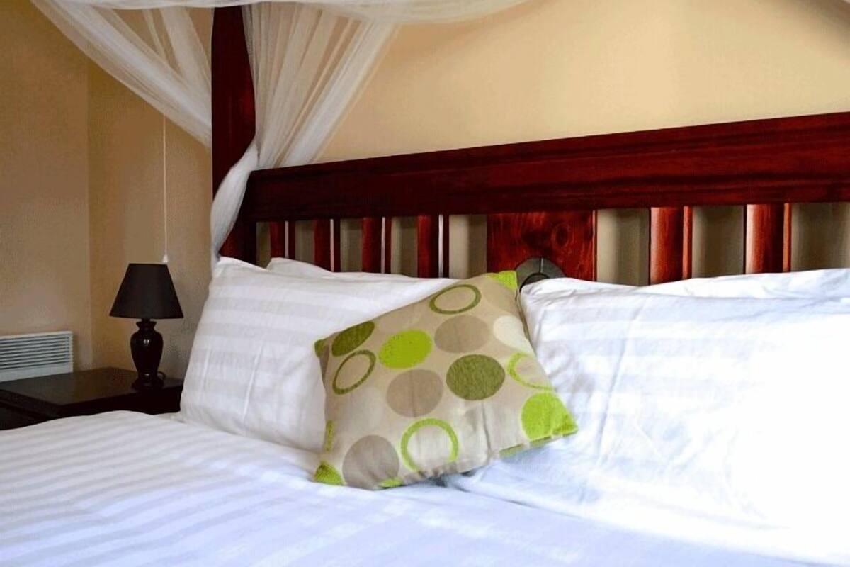 A hotel room with a bed, a nightstand, a lamp, and a canopy bedspread.