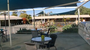 An outdoor patio area with round tables and chairs, a small fountain, and a fenced garden with red flowers. - Tooleybuc Motel (Tooleybuc)