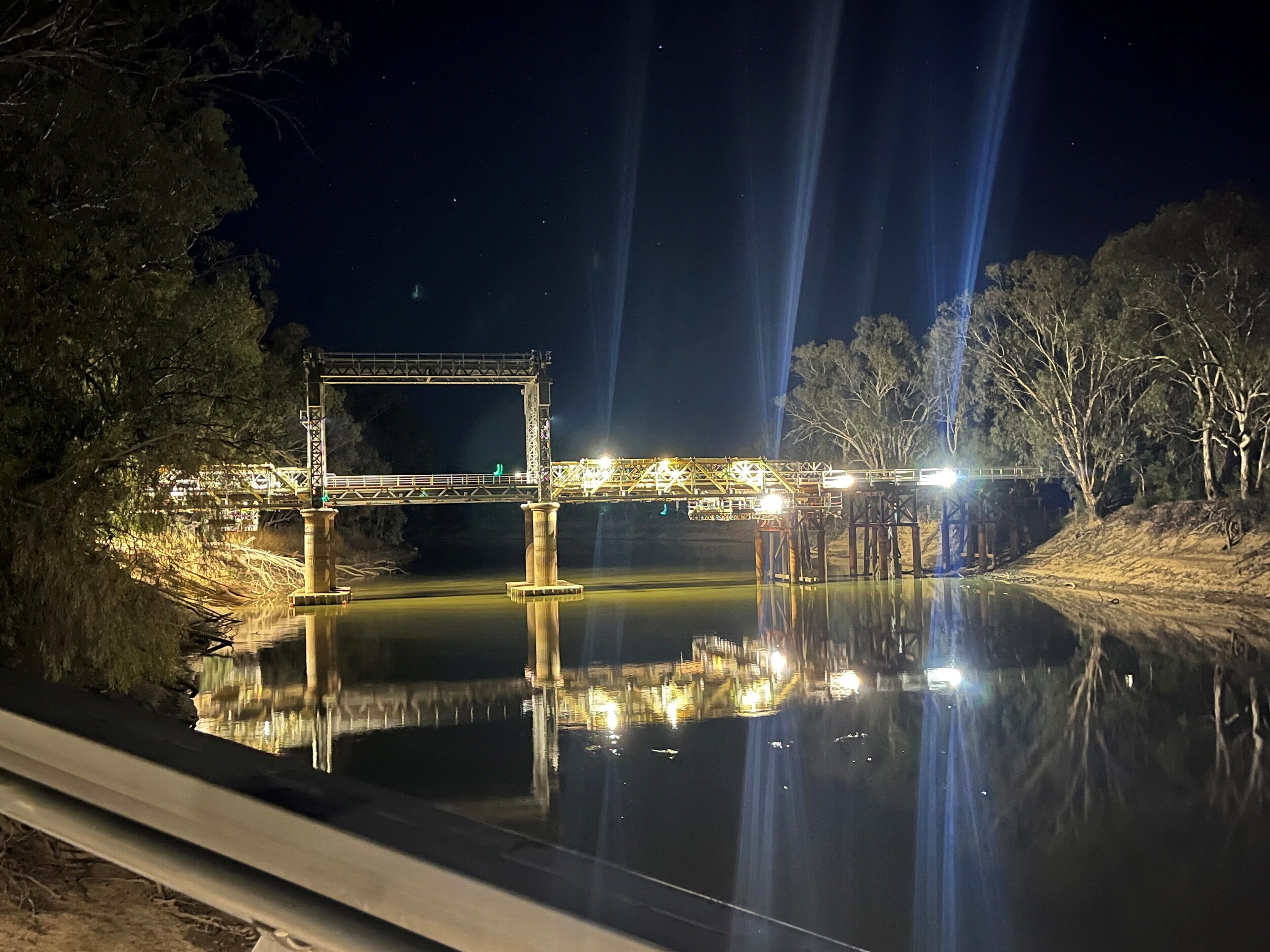 A nighttime view of a bridge over a calm body of water, with its structure and lights clearly visible.