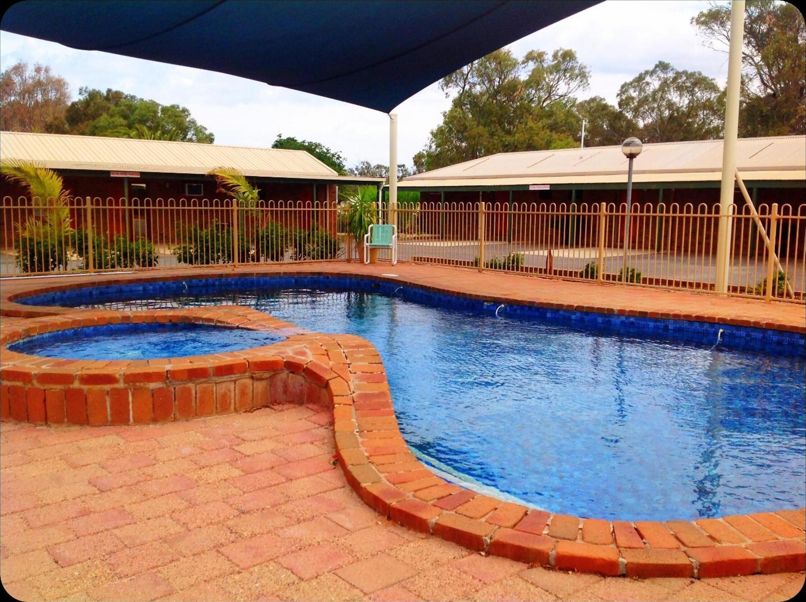 A swimming pool with a brick border, surrounded by a fence and covered by a canopy.