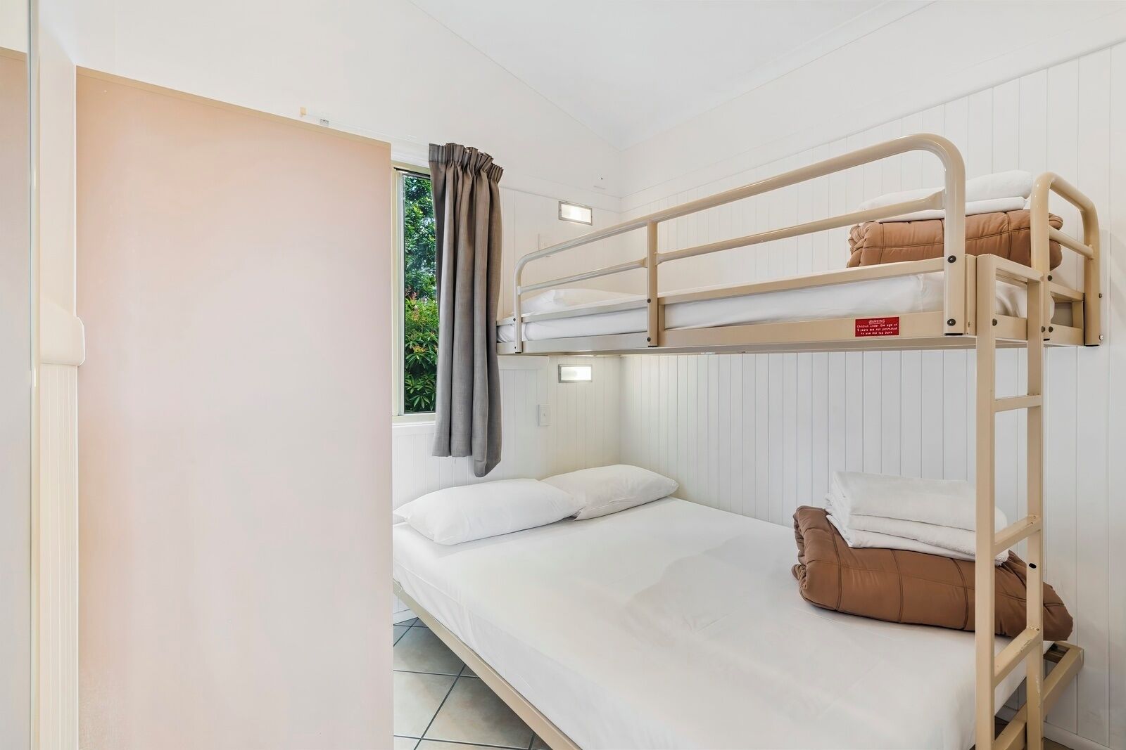 A bunk bed room with a window, curtains, and a door.