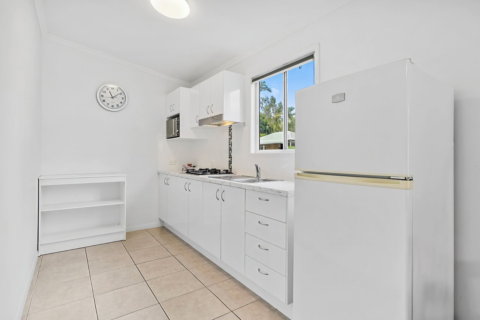 A kitchen with white cabinets, a stove, a sink, and a clock on the wall.