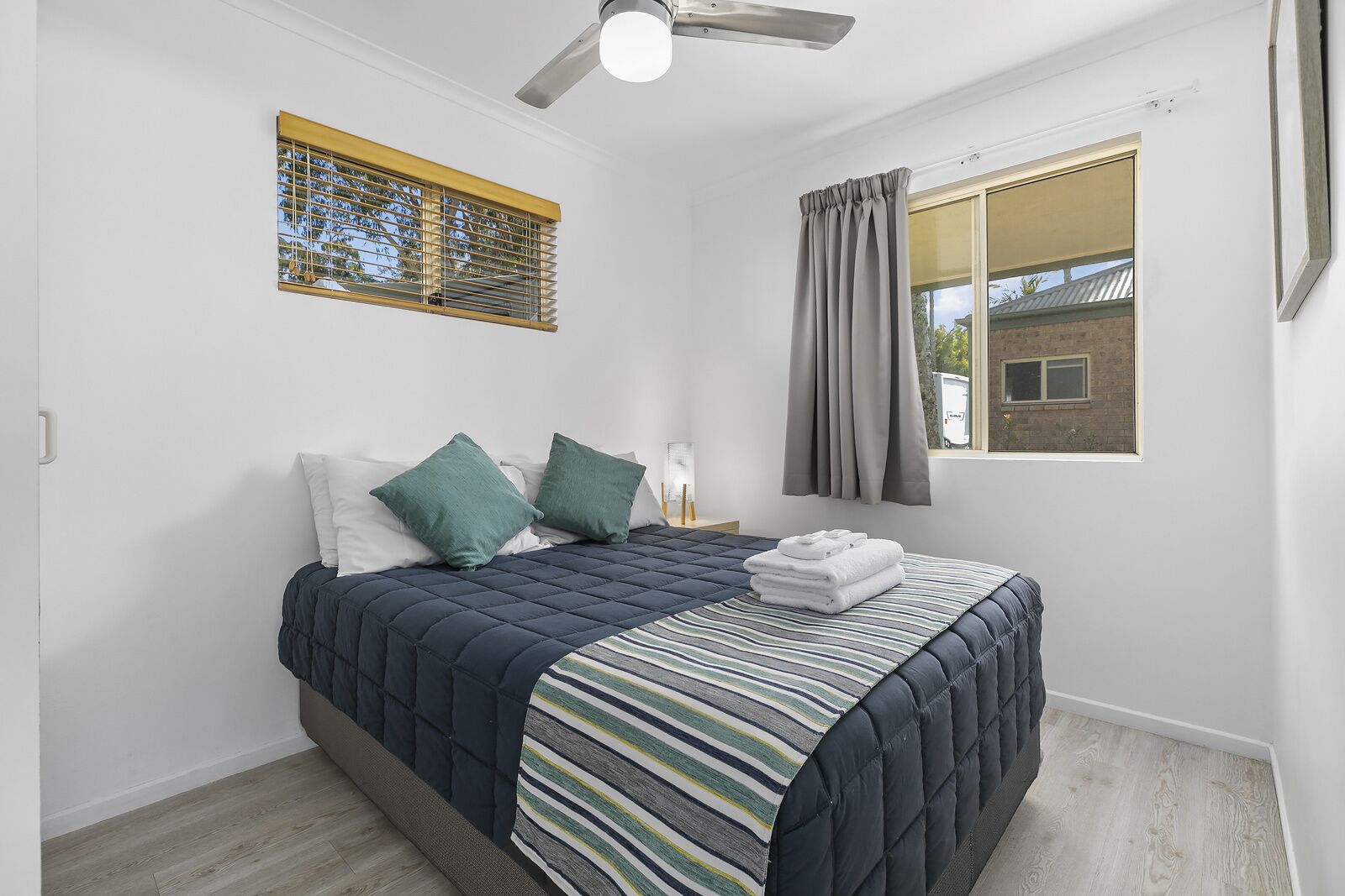 A bedroom with a bed, a ceiling fan, a window with curtains, and a view of a building outside.
