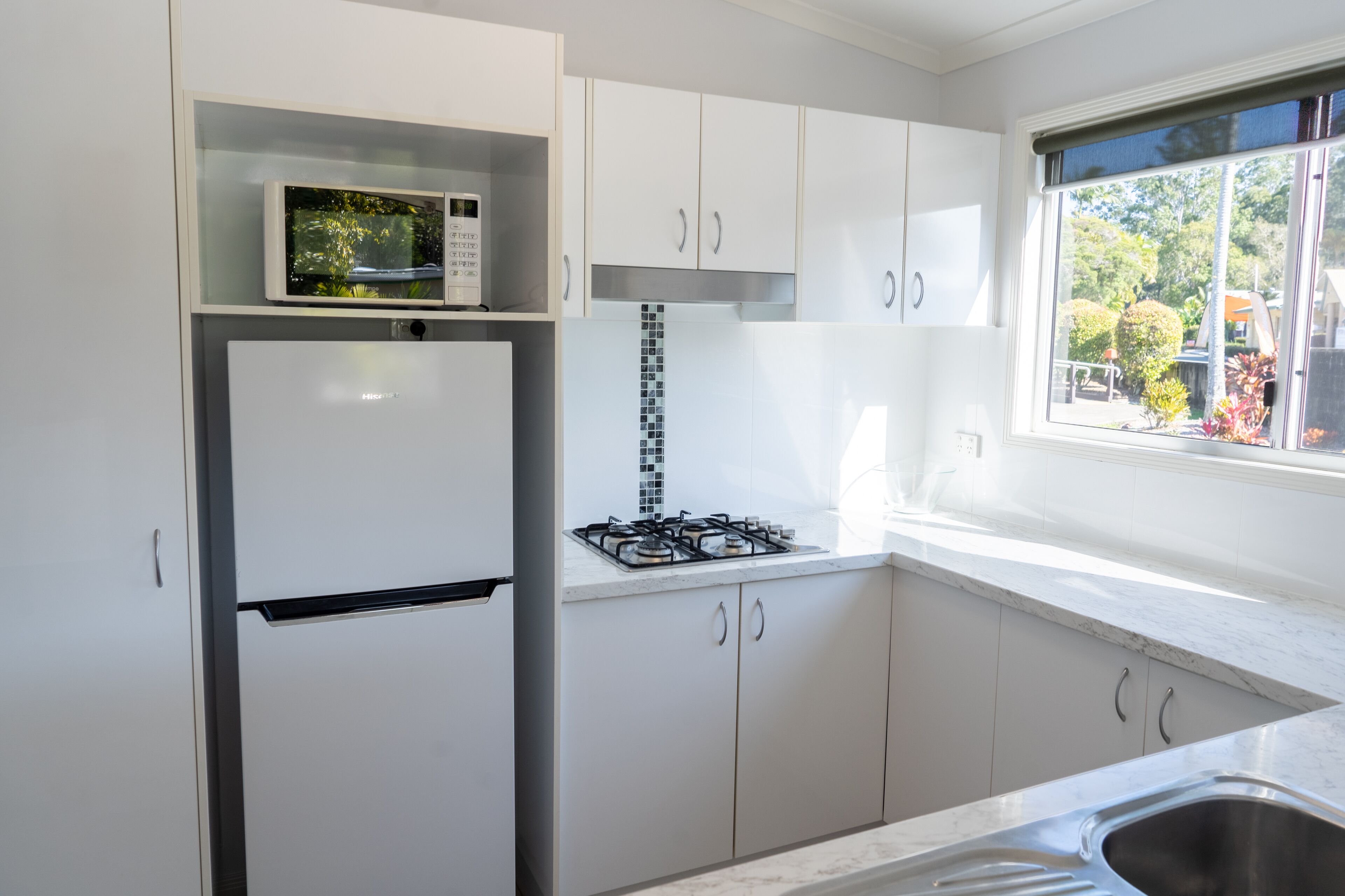 A modern kitchen with white cabinets, a built-in microwave, a gas stove, and a stainless steel sink.