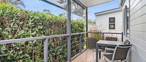 Un espace extérieur abrité, doté d’une table et de chaises, entouré d’une rambarde en métal et d’un feuillage dense.