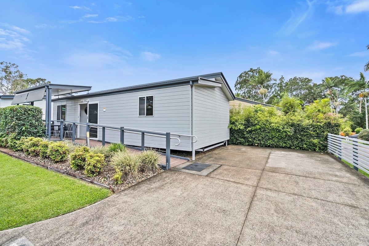 A single-story mobile home with a concrete driveway, a small patio area with a table and chairs, and a well-maintained garden.