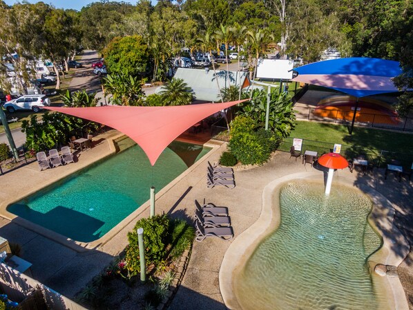 A swimming pool with lounge chairs and a water feature, surrounded by greenery and shaded by large umbrellas. - Ingenia Holidays Noosa (Tewantin)