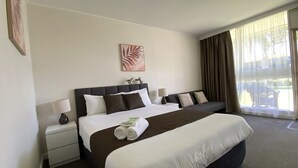 A hotel room with a large bed, a bedside table, a lamp, a window with curtains, and a wall art piece. - Warrina Motor Inn Wodonga CBD (Wodonga)