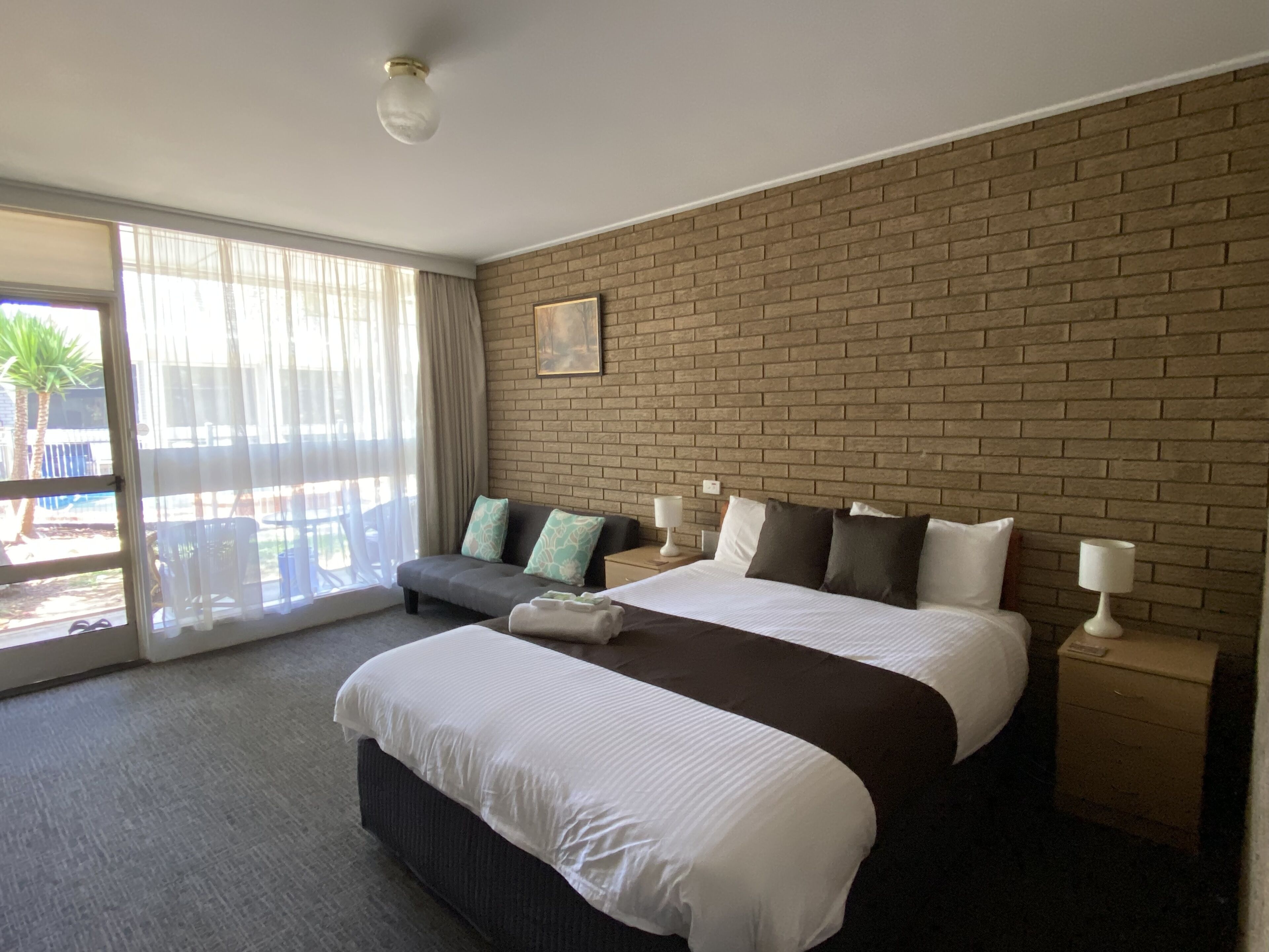 Habitación de hotel con una cama grande, un sofá, un ventanal corredero al exterior y una pared de ladrillo.