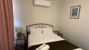 Une chambre d’hôtel avec un lit, une table de chevet, un appareil de climatisation, un tableau encadré au mur et un rideau.
