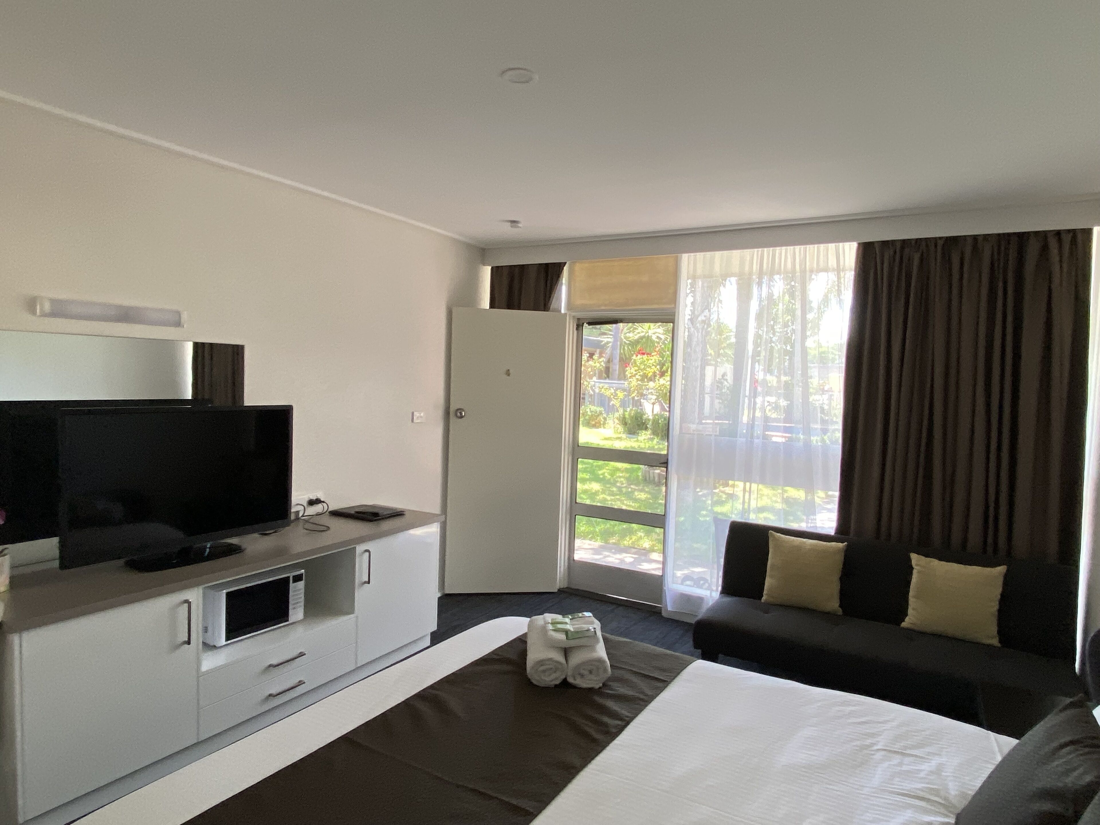 Una habitació d'hotel amb llit, televisió, escriptori i finestra amb cortines.