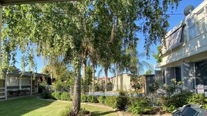 A courtyard with a lawn, a tree, outdoor furniture, and a building with a satellite dish. - Warrina Motor Inn Wodonga CBD (Wodonga)