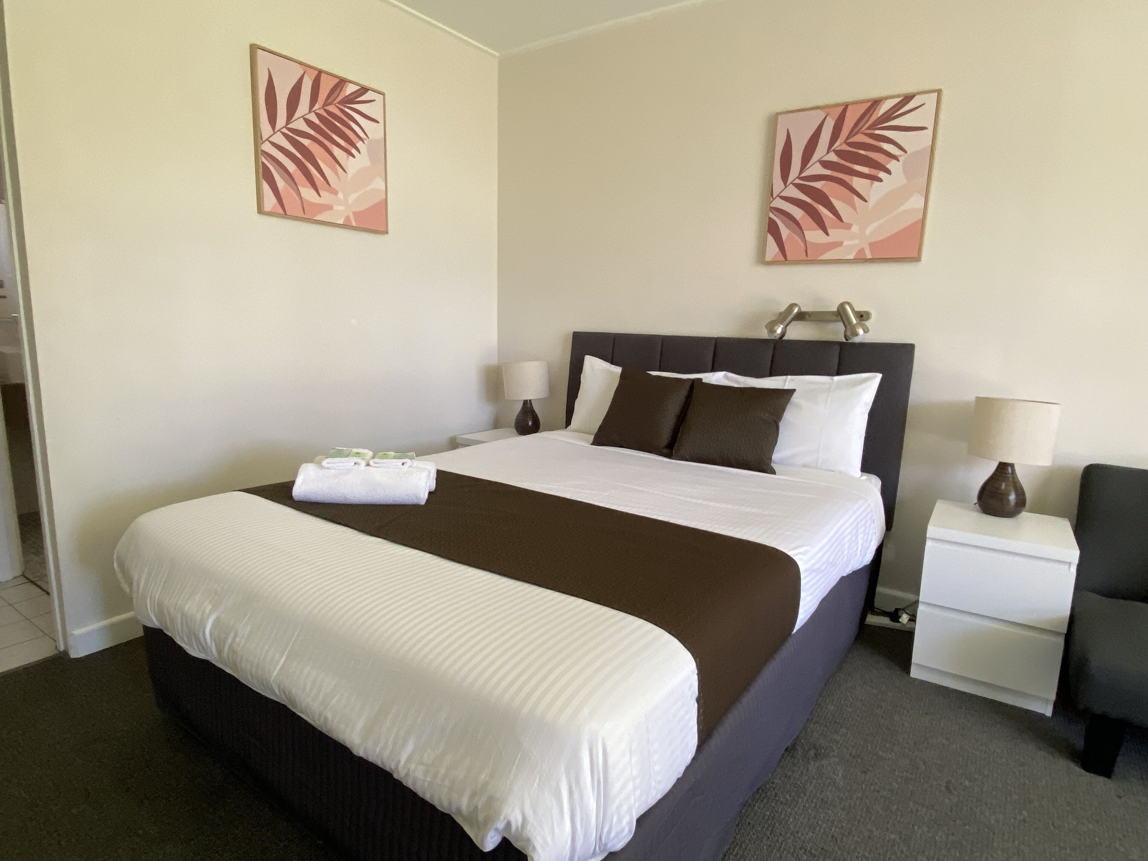 A hotel room with a large bed, two bedside tables, a chair, and two wall-mounted lamps.