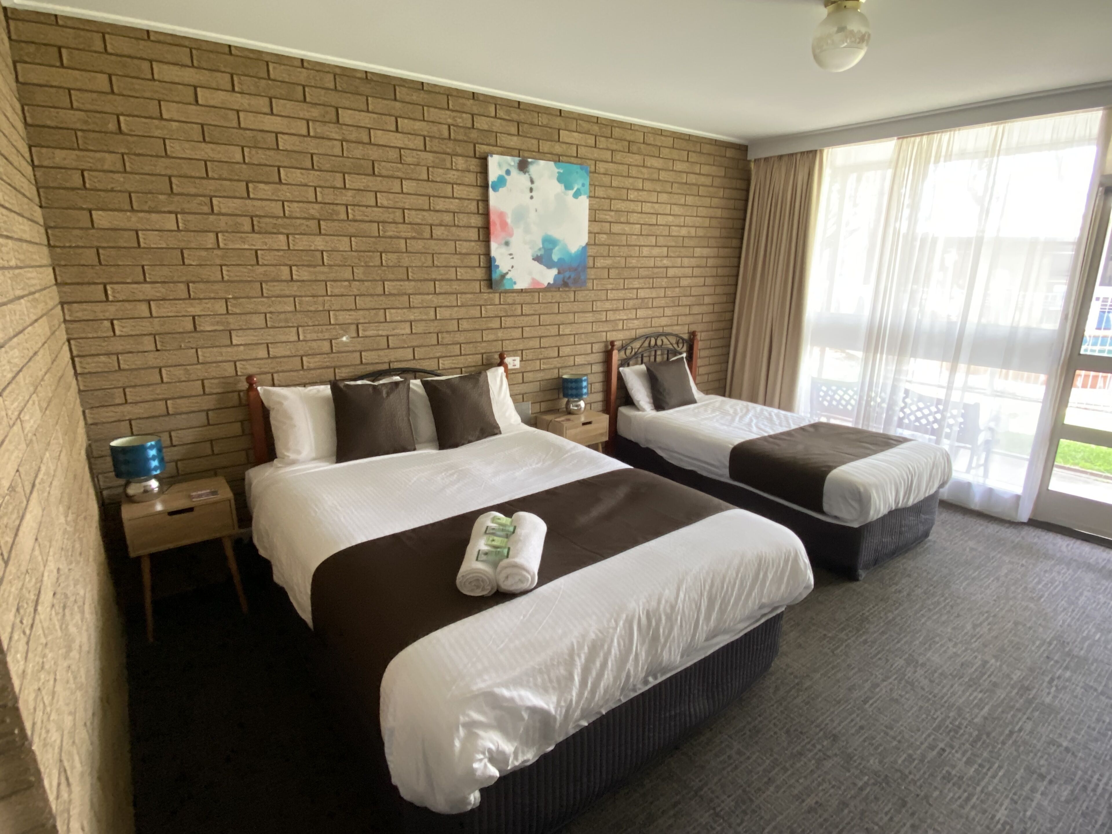 Habitación de hotel con dos camas, una pared de ladrillo, un cuadro y vistas al exterior.