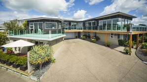 A modern building with large glass windows, a covered patio area, and a variety of potted plants. - Tahi Lodge - Matakana Coast (Snells Beach)