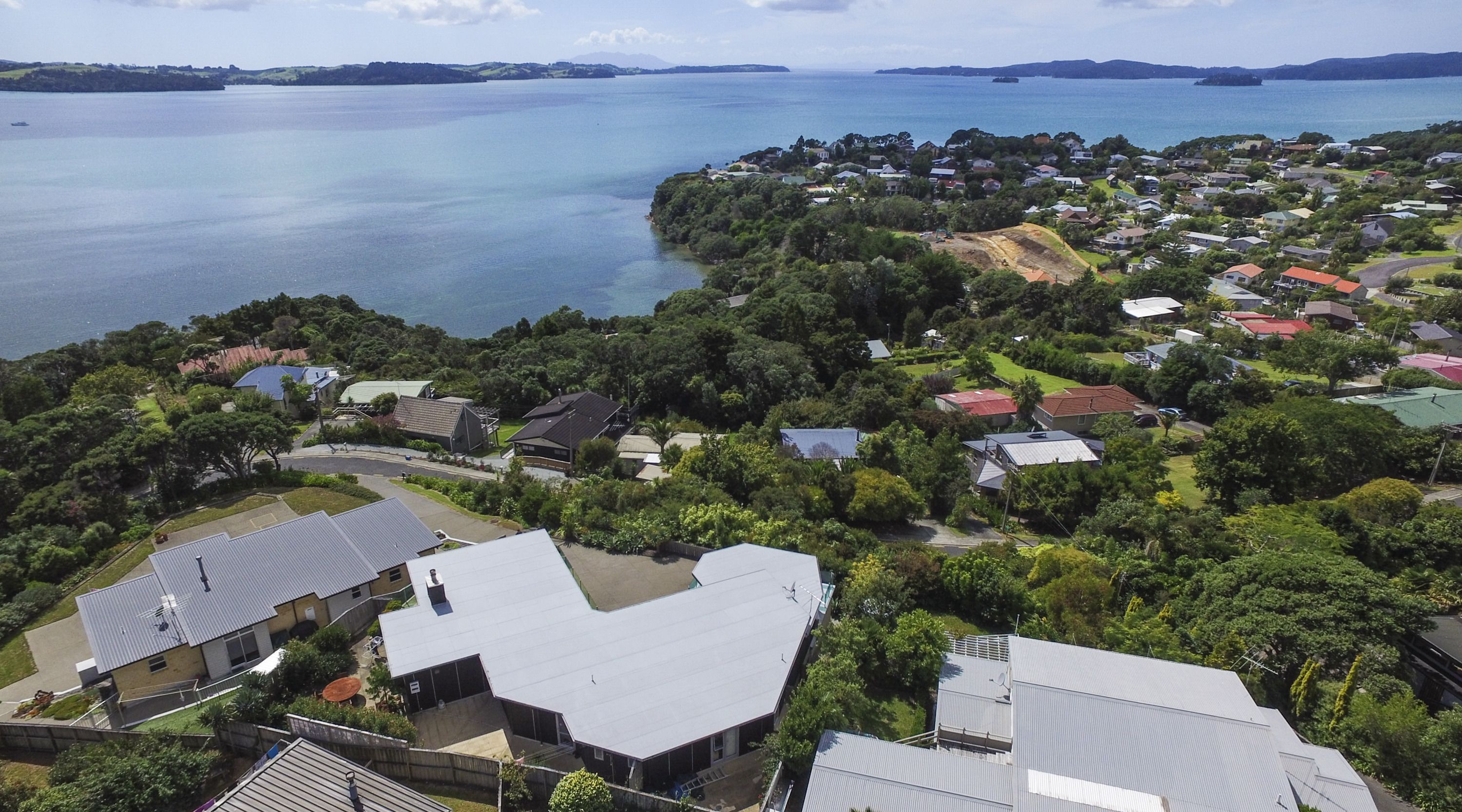 An aerial view of a residential area with houses, a large body of water, and a hilly landscape in the background.