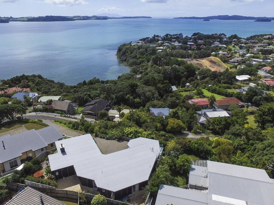 An aerial view of a residential area with houses, a large body of water, and a hilly landscape in the background.