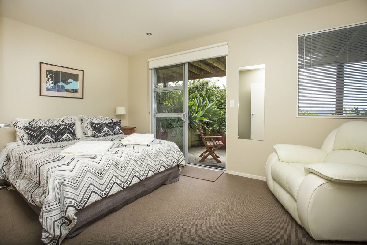 A bedroom with a bed, a chair, a door leading to a balcony, and a framed picture on the wall.