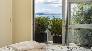 A bedroom with a bed, a view of the sea, and a balcony with potted plants. - Tahi Lodge - Matakana Coast (Snells Beach)