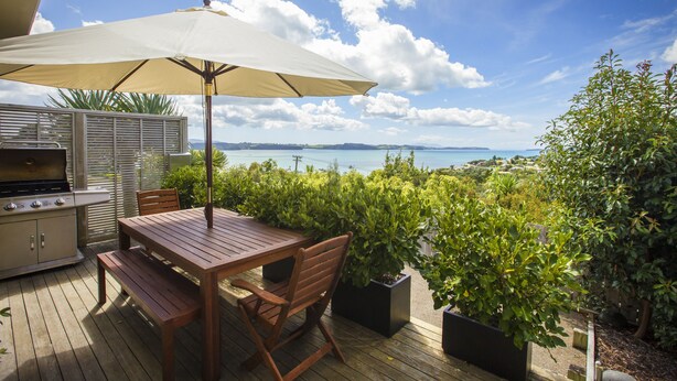 An outdoor patio with a wooden table, chairs, a grill, and an umbrella. - Tahi Lodge - Matakana Coast (Snells Beach)