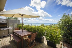 An outdoor patio with a wooden table, chairs, a grill, and an umbrella.