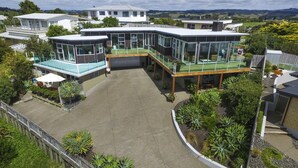 A modern house with a large patio, glass-enclosed rooms, and a view of the surrounding landscape. - Tahi Lodge - Matakana Coast (Snells Beach)