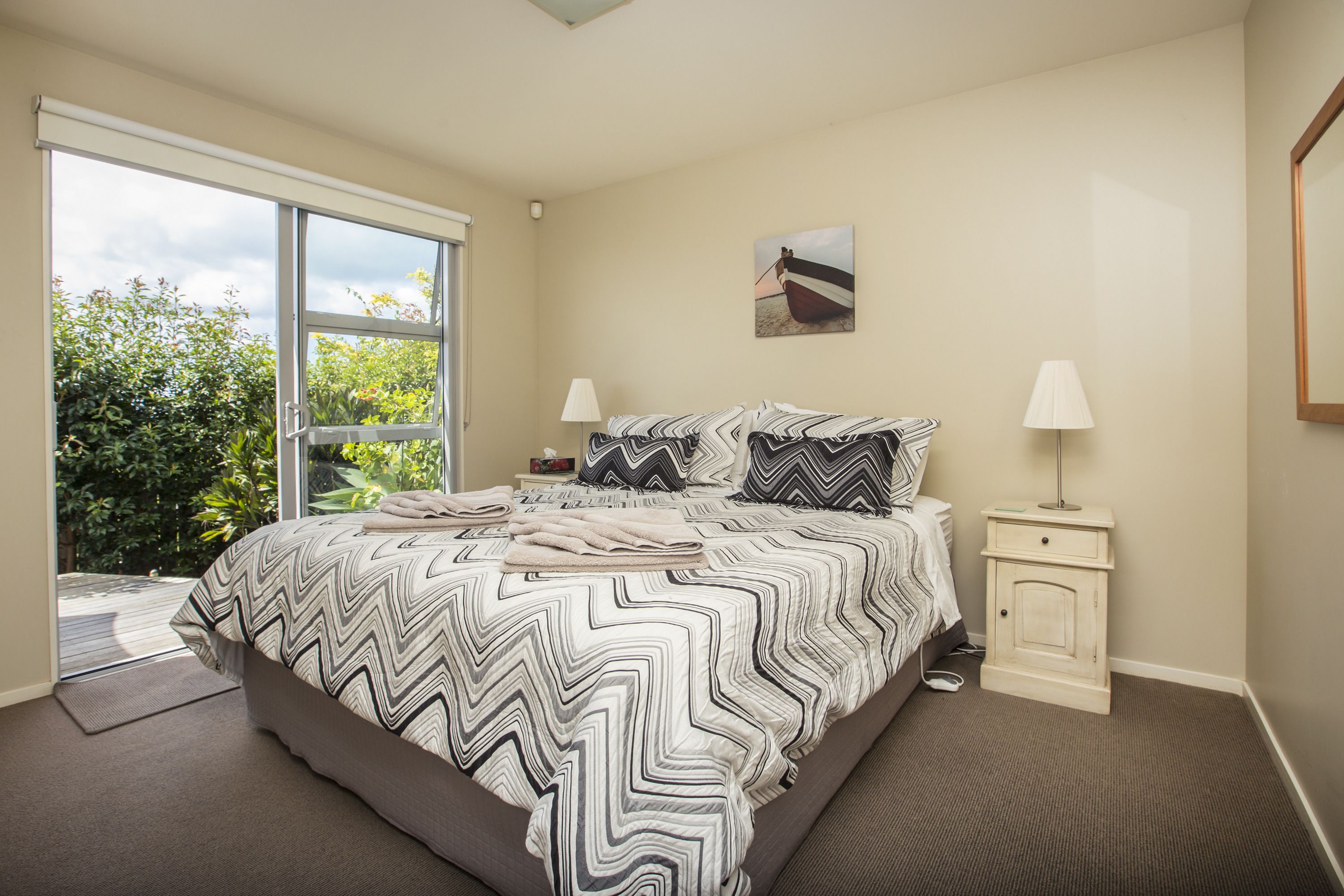 A bedroom with a large bed, two bedside tables, a window, and a painting on the wall.
