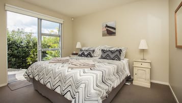 A bedroom with a large bed, two bedside tables, a window, and a painting on the wall.