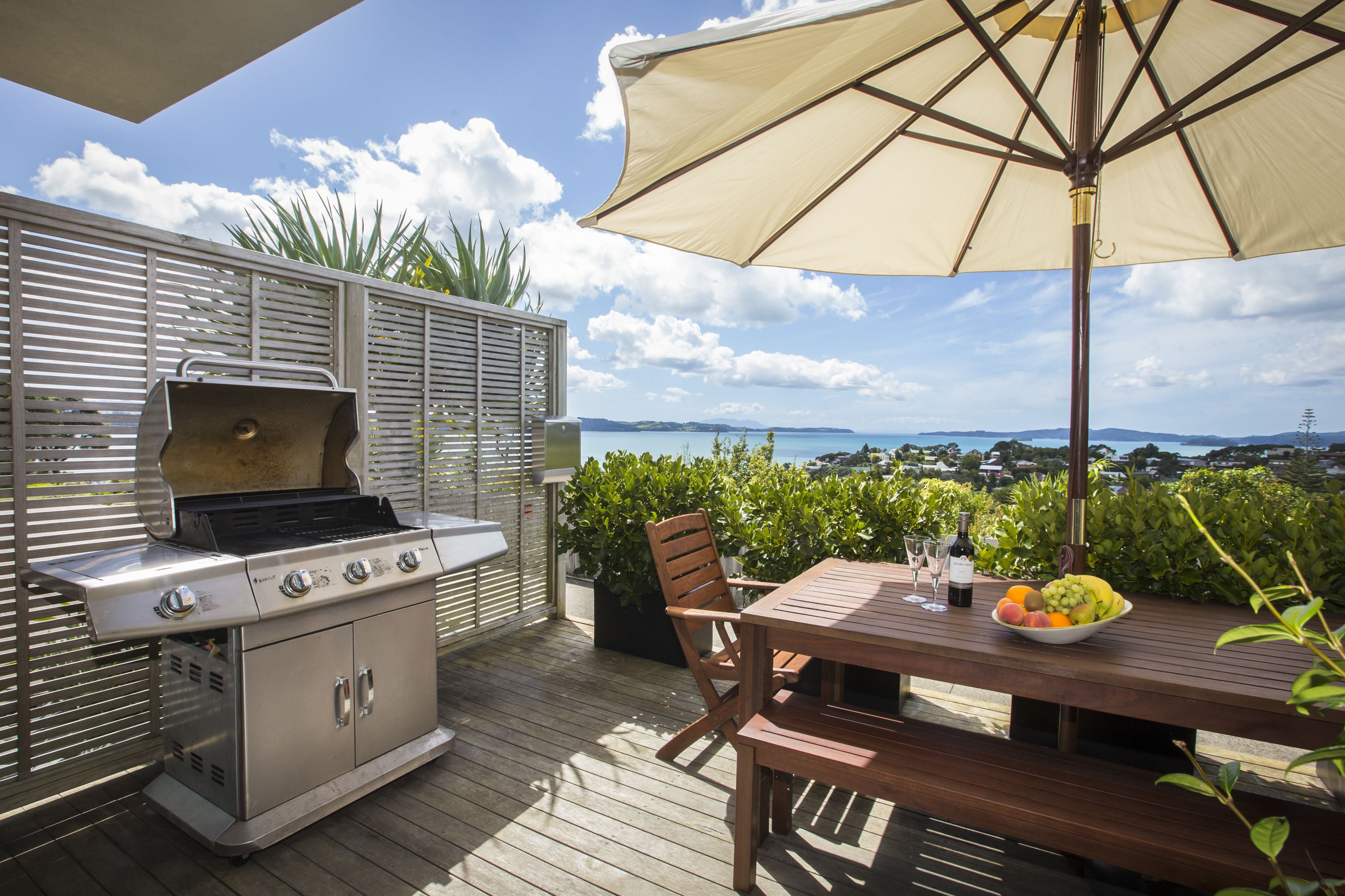 En udendørs terrasse med grill, træbord og parasol.