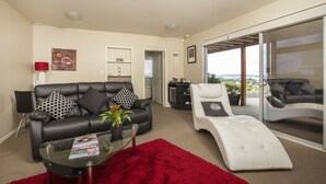 A modern living room with a black leather sofa, a white lounge chair, and a glass coffee table. - Tahi Lodge - Matakana Coast (Snells Beach)