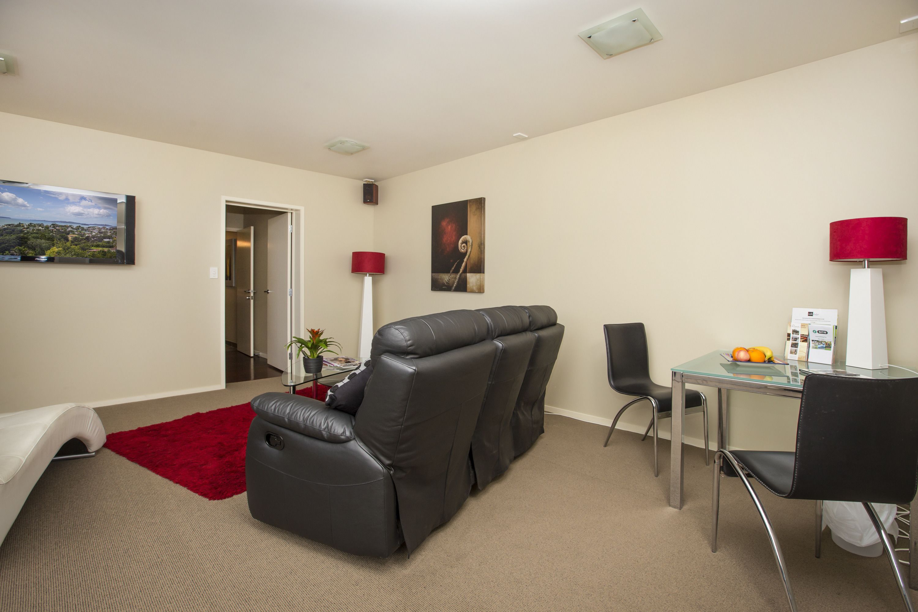 A modern living room with a leather sofa, a glass coffee table, and a red rug.