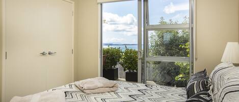 A bedroom with a bed, a window with a view, a door, and a potted plant.