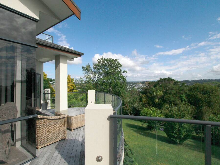A balcony with a glass door, wicker furniture, and a view of a green landscape.